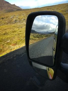View in side mirror of a car. Empty road in front of a mountain range with .. Stock Photos