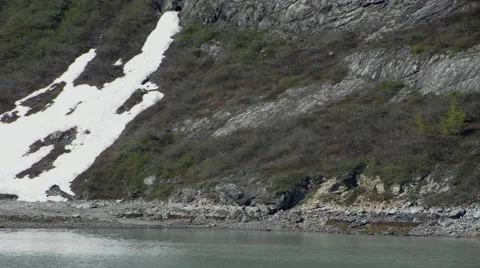 View of the side of a mountain partially covered with snow, water at the base, Stock Footage 52216334