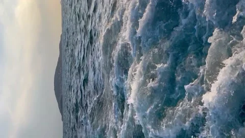 View from the side of the ship to the sea foam and island - Vertical stock video Stock Footage 239640893