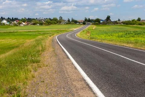 View of the small asphalt road in the countryside with blue sky and cumulus.. Stock Photos