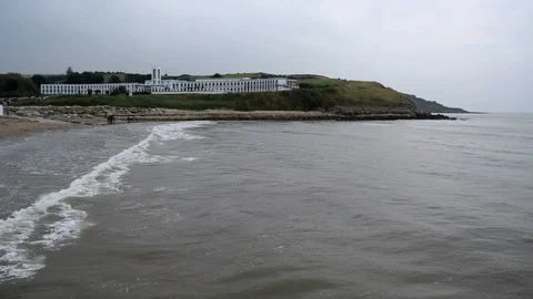 View from small pier - waves breaking onto beach and cliffs with hotel Stock Footage 106092146