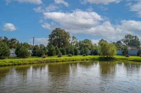 View of a small quiet pond, in the background trees and old houses against a Stock Photos