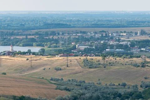 View of a small town by a river surrounded by fields and hills during a cle.. Stock Photos