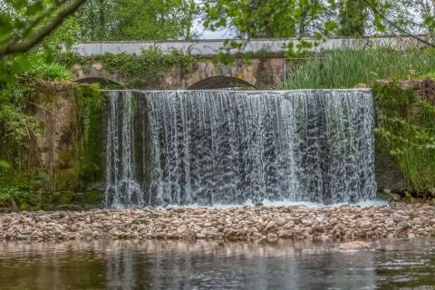 View of small waterfall in river in forest, with old bridge as background Foto stock