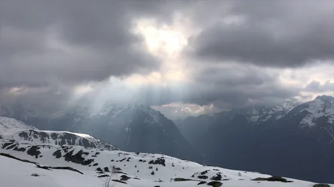 View of the snow-capped mountains and the sun piercing the clouds Видео 74134252