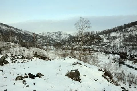 View of a snow-covered valley surrounded by high mountains under a cloudy sky Stock Photos