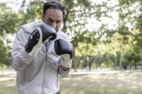 View of a sporty guy posing with boxing gloves in a public park after the tra Stock Photos
