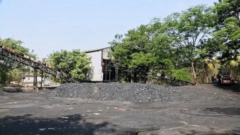 A view of stacked charcoal heaps and a conveyor machine at the factory yard Stock Footage 245090981