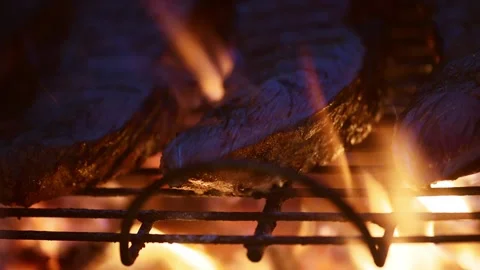 View of steaks grilling over open flames on a barbecue. Vídeo Stock 335608628