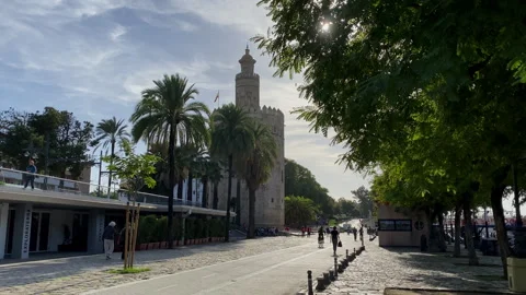 View from a stone arch onto Sevilla riverside promenade with cyclists and soft 스톡 동영상 327504247
