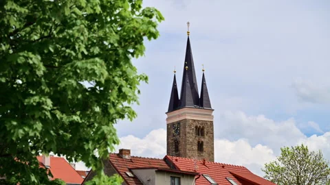View of a stone church tower with a clock and a black spire above red tiled Stock Footage 342242922