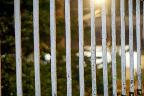 View of sturdy vertical white metal fence bars under a warm evening streetlight Stock-Fotos