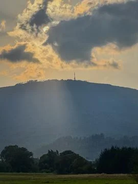 A view of the sun setting between the clouds over a mountain with an antenn.. Stock Photos