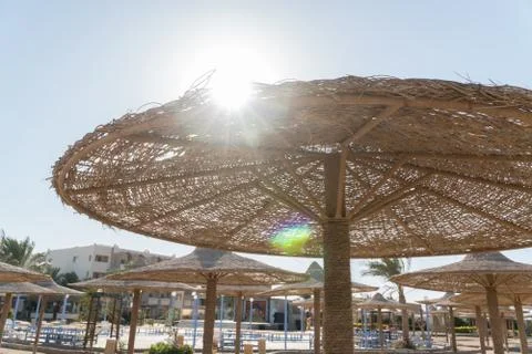 View of the sun from under the umbrella. Wicker beach umbrellas in the backgr Stock Photos