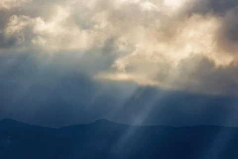 View of sunbeams going through dense dark clouds, in a rainy afternoon, over  Stock Photos