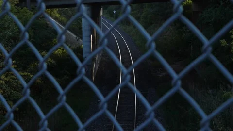 View of sunlit railroad tracks through defocused chainlink fence. Stockbeeldmateriaal 165073057