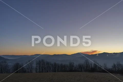 A view of the sunrise surrounded by small mountains Stock Photos