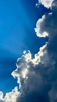 View of the sun's rays breaking through white clouds against a blue sky Stock Photos