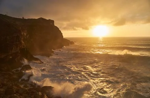 View of the sunset and the old lighthouse on a rock with a fortress on the coast Stock Photos