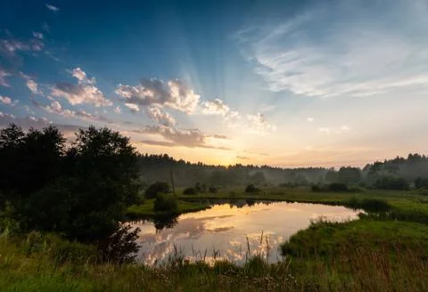 View of a sunset rays under the forest lake at the meadow Stock Photos