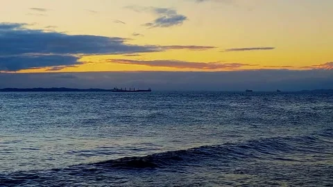 View of a sunset on the shore of a beach with boats in the background Stock Footage 320056894