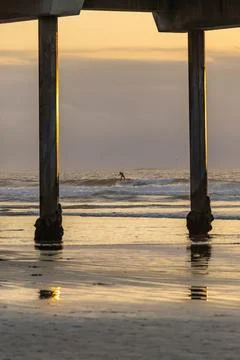 View of a surfer in the ocean between the columns of a pier Stock Photos