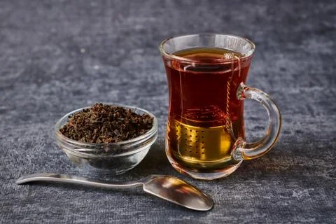 View of tea cup with sieve next to socket with brew and teaspoon on grey back Stock Photos
