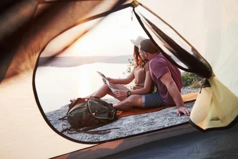 View from tent of couple with map lying a view of lake during hiking trip. av Stock Photos