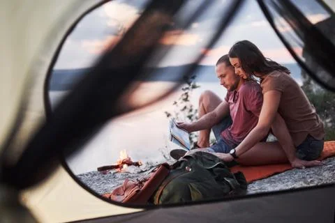 View from tent of couple with map lying a view of lake during hiking trip. av Stock Photos