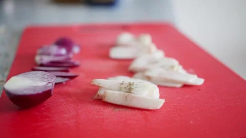 View of thinly sliced white lard and red onions arranged on a red cutting board Stock Footage 304683361