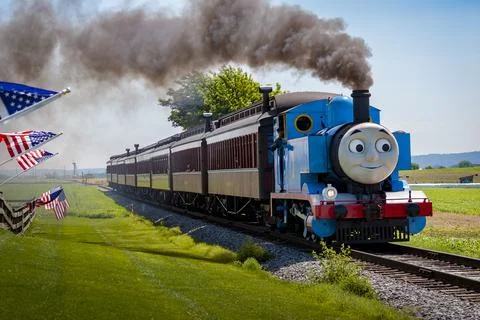 View of Thomas the Train Pulling Passenger Cars While Passing American Flags on Stock Photos