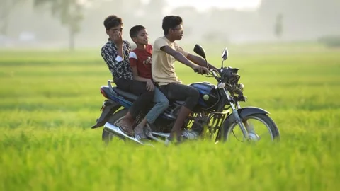 View of three young men on a motorcycle in a green field, Bangladesh. 動画素材 335651056