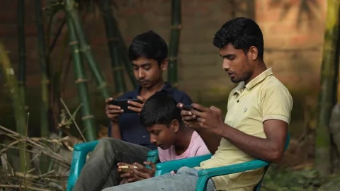View of three young men using smartphones outdoors, Bangladesh. Video stock 335025575