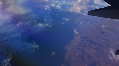 View through an airplane window above the mountains in the blue sky in clouds 库存影片 68769793