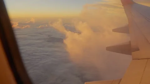 View through airplane window flying above clouds at golden hour sunrise 스톡 동영상 338145170