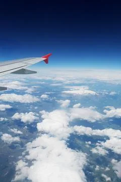 A view through an airplane window. Visible wing, clouds over land and space Stock Photos