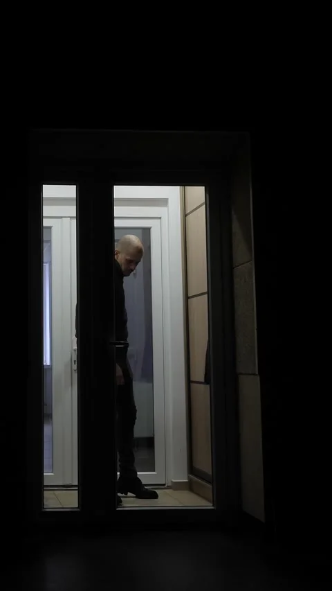 View through the backlit glass doors a man enters a dark room. Stock Footage 324791370