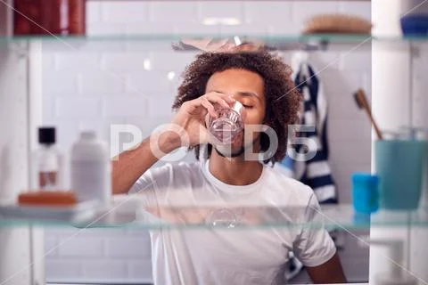View Through Bathroom Cabinet Of Man Drinking Glass Of Water Stock Photos