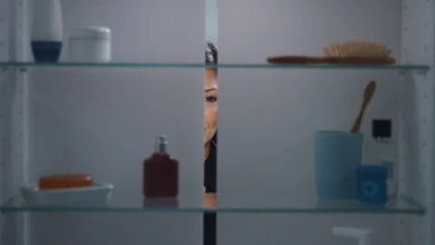 View Through Bathroom Cabinet Of Mature Woman Spraying Perfume From Bottle Stock Footage