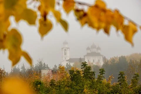 View through blurred branches of trees in autumn on the church in the fog Stock Photos