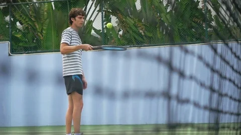 View through the blurred grid of handsome man beats the tennis ball with the Stock Footage 85014314