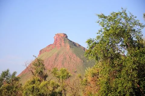 A view through the branches of trees to a high red hill with the remains of a Foto stock