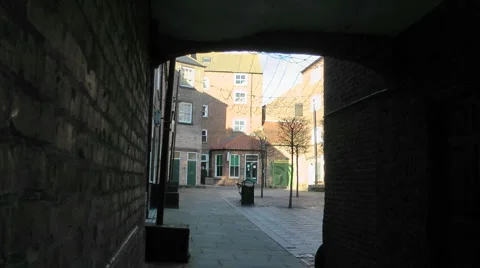 View through brick arch passage into sunlit urban court yard Stock Footage 1060344