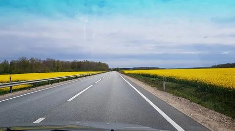 View through the car window on the highway passing between the rapeseed field Stock-Fotos