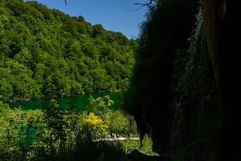 View through dark rocky cave shadow towards green lake and forest in Plitvi.. Stock Photos