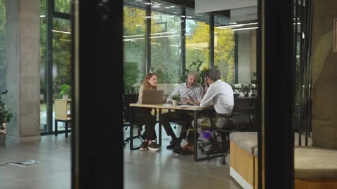 A view through a glass partition shows a modern, busy office interior. 스톡 동영상 325774373