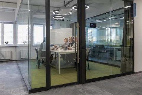 A view through a glass partition shows a modern, busy office interior. Busi.. Stock Photos