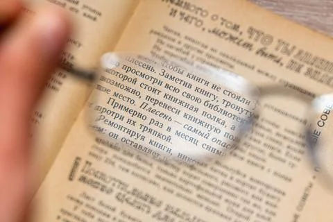 View through glasses in hand on a text in the book Stock Photos