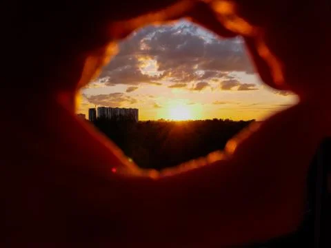 View through hand in oval shape over dramatic colorful sunset with red hot su Stock Photos