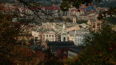 View through the leaves on a ferris wheel and a city center, church and rooftops Stock Footage 222093593